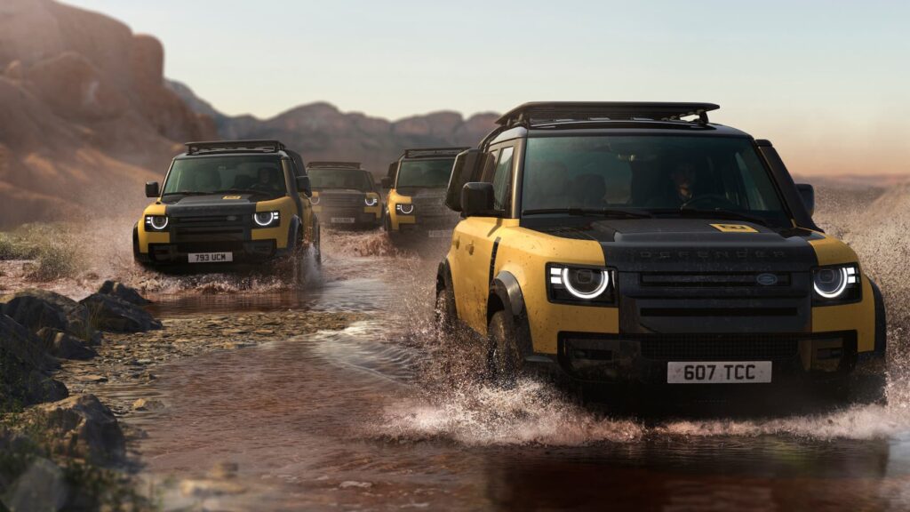 Close-up of Defender 110 Trophy Edition in Deep Sandglow Yellow with Gloss Black accents, featuring expedition roof rack and rugged wheel arch protection