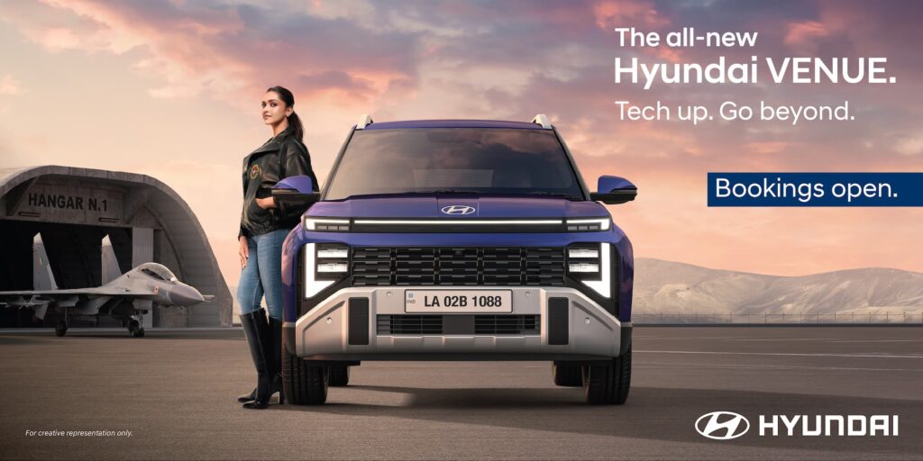 Front view of the all-new 2025 Hyundai Venue in Mystic Sapphire blue, parked near an aircraft hangar, with text 'Bookings Open'