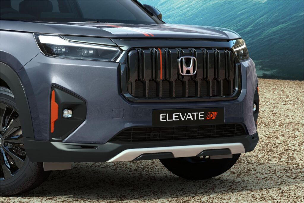 Close-up of the Honda Elevate ADV's all-black front grille, highlighted by a single vertical active orange accent strip and orange trim around the fog light housings. The lower bumper features a silver garnish.